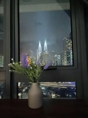 a vase with flowers in a window with a city at CLS 16B KLCC Balcony View Studio in Kuala Lumpur