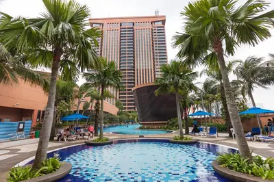 a pool with palm trees in front of a hotel at Suites at TimesSquare by Plush in Kuala Lumpur