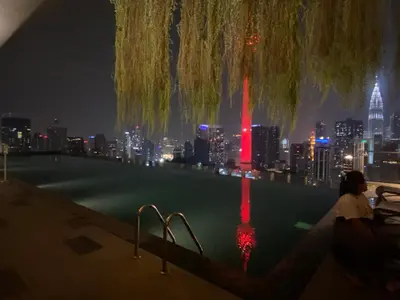 a woman sitting on the edge of a swimming pool at night at Staybliss At Ceylonz Suites in Kuala Lumpur