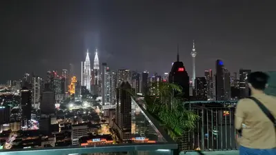 a man looking at a city skyline at night at Hostel At Regalia Residence in Kuala Lumpur