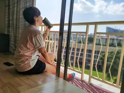 a woman sitting on the floor drinking from a cup on a balcony at Tatami MUJI Relax 5p City center Staycation MRT in Kuala Lumpur