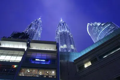 three tall skyscrapers are lit up at night at OYO 115 Hotel Safari 1 in Kuala Lumpur