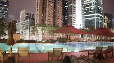 a pool with chairs and umbrellas in a city at night at Spacious Family Apt 3-Min Walk to KLCC MRT RO Water Baby Crib Home Cinema Projector in Kuala Lumpur