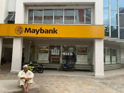 a man sitting on a bench in front of a may bank building at Hotel grand orchard in Kuala Lumpur
