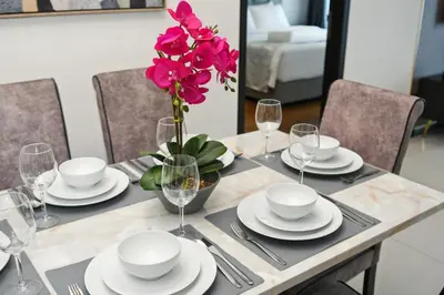 a table with plates and glasses and a vase with pink flowers at Luxe Suite in Kuala Lumpur