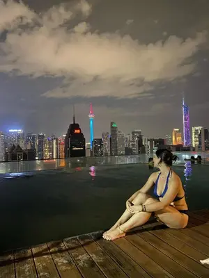 a woman in a bikini sitting on the edge of a city skyline at KL Infinity Luxury Skypool hostel in Kuala Lumpur