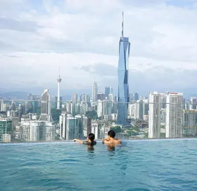 two people in a infinity pool with a view of the city at Riveria City Kuala Lumpur By Nest Suites in Kuala Lumpur