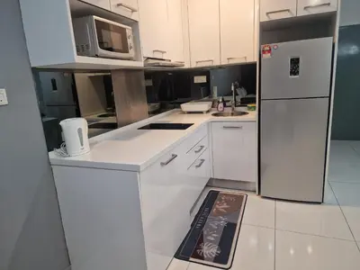 a white kitchen with a refrigerator and a sign on the floor at Summer Luxury Suites KlCC by ATIQ in Kuala Lumpur