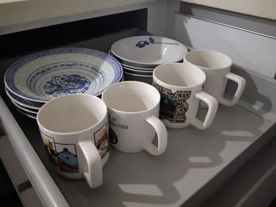 four cups and plates are sitting on a shelf at Camellia Serviced Suites in Kuala Lumpur