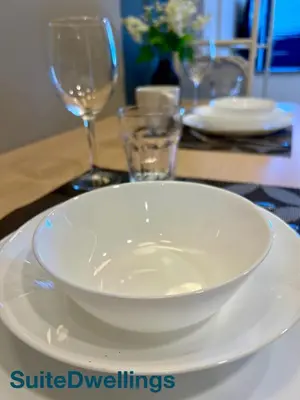 a white bowl on a plate on a table with glasses at TheRiv Boutique Suites at Riveria City KL Sentral by Suite Dwellings in Kuala Lumpur