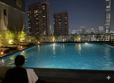 a man sitting next to a large swimming pool at night at Luxury Fairlane Residence Suites Kuala Lumpur by AZI BNB in Kuala Lumpur