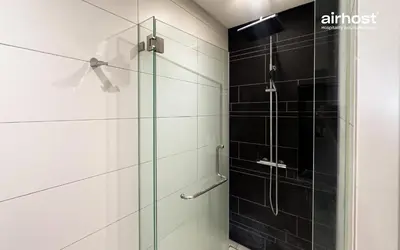 a glass shower in a bathroom with black tiles at Anggun Residence KLCC by Airhost in Kuala Lumpur
