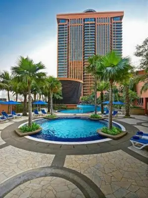 a resort pool with palm trees and a tall building at KL Suite at Times Square in Kuala Lumpur