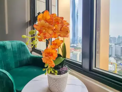 a vase with orange flowers on a table in front of a window at KL City Designer Studio in Ceylonz with KL118 Tower View CityNest in Kuala Lumpur