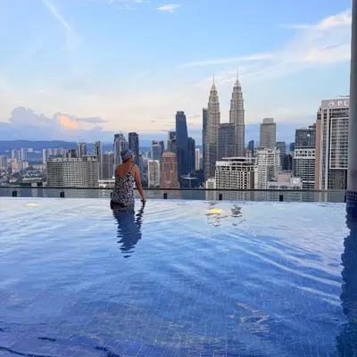 a woman standing on top of a infinity pool with a city skyline at Luxe Colony By Urban Haven in Kuala Lumpur