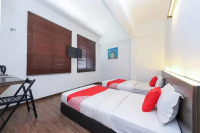 two beds in a room with a table and a desk at Hotel O Madras in Kuala Lumpur