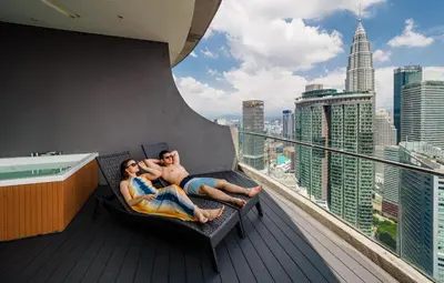 two people laying on a balcony with a view of the city at The Penthouse KLCC in Kuala Lumpur