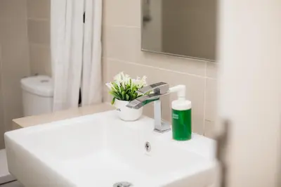a bathroom sink with a green bottle of soap and flowers at Binjai 8 KLCC by PSM Luxury Suites in Kuala Lumpur