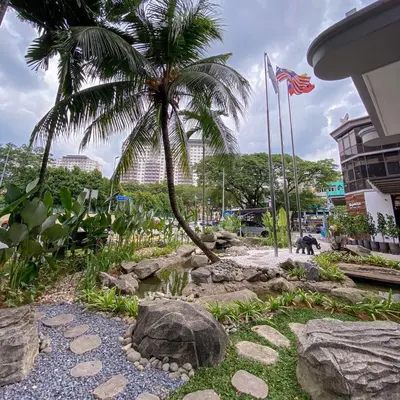 a garden with rocks and a palm tree and a flag at Hotel Maluri in Kuala Lumpur