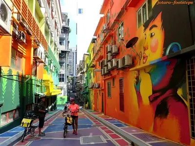 two people riding bikes down a city street with a painting at Inspired Homes @ KLCC Soho Suite in Kuala Lumpur
