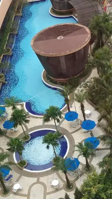 an overhead view of a pool with palm trees and blue umbrellas at KL Times Square Apartment in Kuala Lumpur
