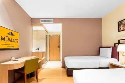 a hotel room with a bed and a desk and a bed and a table at MPalace Hotel KL in Kuala Lumpur
