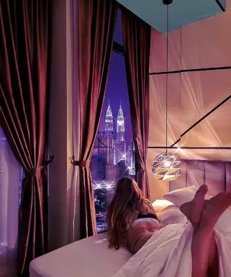 a woman laying in bed looking out of a window at WGS Suites at KLCC in Kuala Lumpur