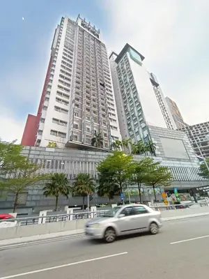 a white car driving down a city street with tall buildings at Taragon Apartment - KL ,Malaysia in Kuala Lumpur