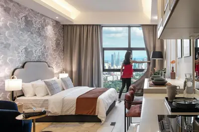 a hotel room with a bed and a woman looking out the window at AMI Suites - Arte Mont Kiara in Kuala Lumpur