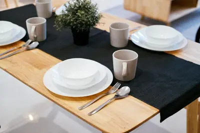 a wooden table with white plates and silverware on it at Arte Mont Kiara by CozyNest in Kuala Lumpur