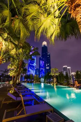 a pool with palm trees and a city at night at Agile Delima Residence Bukit Bintang in Kuala Lumpur