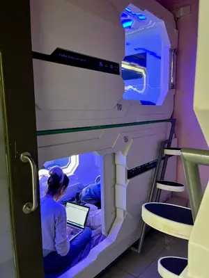 a woman sitting on a bed in a room with a laptop at Bestow Capsule Hostel in Kuala Lumpur