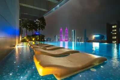 a row of chaise lounges in a swimming pool at night at MOONWAY SUITES At EATON KLCC in Kuala Lumpur