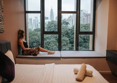 a woman sitting on a window seat looking out at the city at Ceylonz KLCC by Mana-Mana in Kuala Lumpur