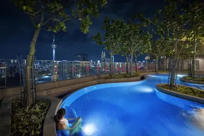 a man sitting in a chair next to a swimming pool at night at S27- Bukit Bintang Robertson 3BR Suite with Netflix in Kuala Lumpur